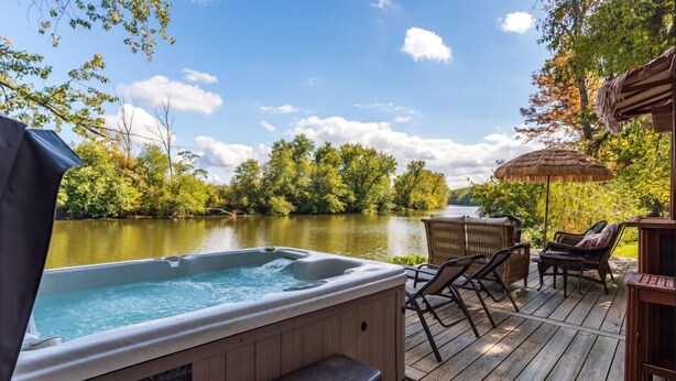 Ein Whirlpool auf einer Holzterrasse mit Blick auf einen Fluss und Bäume.