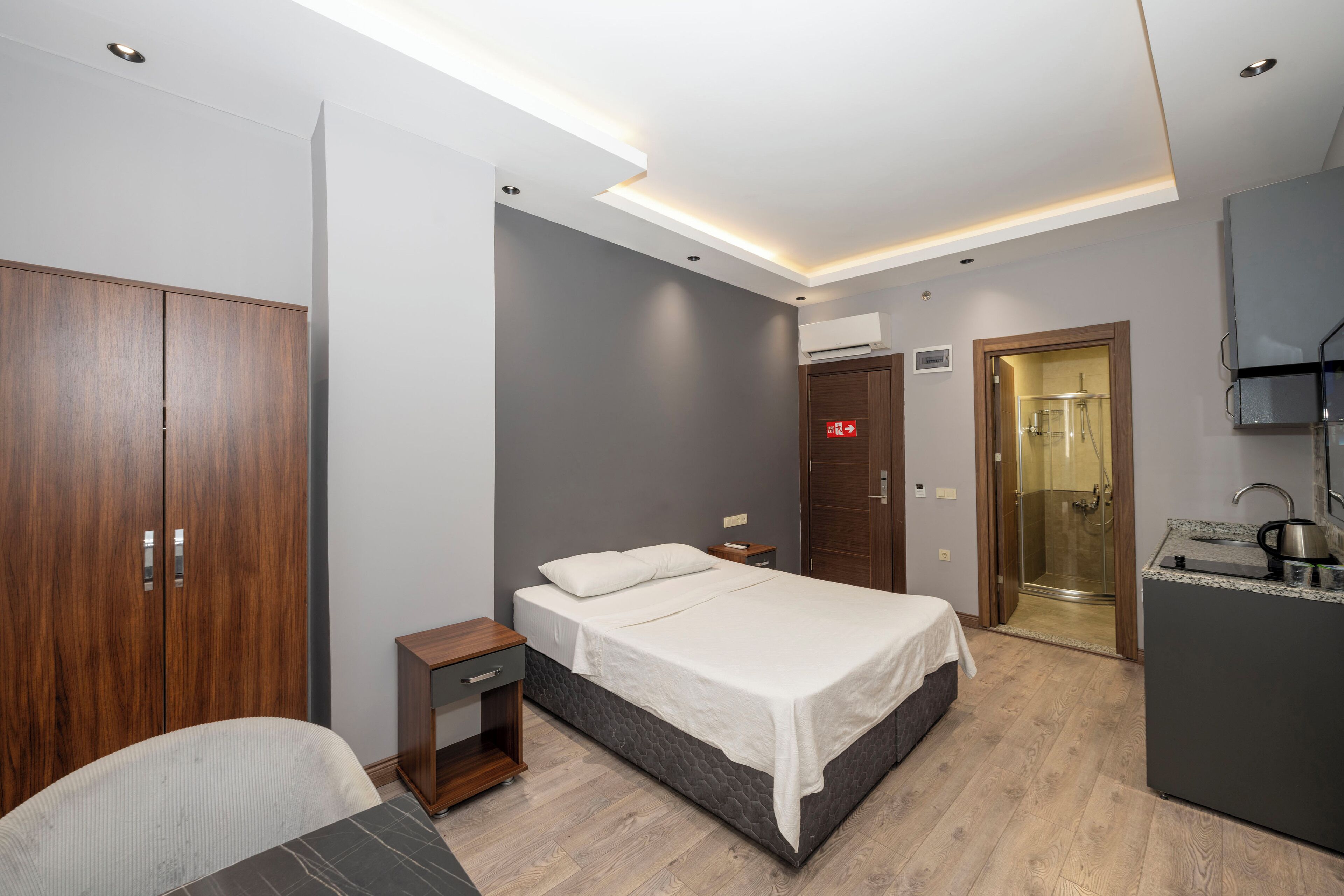 A modern bedroom with a bed, wooden wardrobe, bedside table, and a shower area.