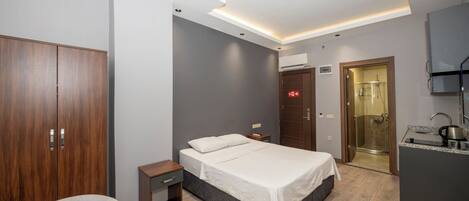 A modern bedroom with a bed, wooden wardrobe, bedside table, and a shower area.