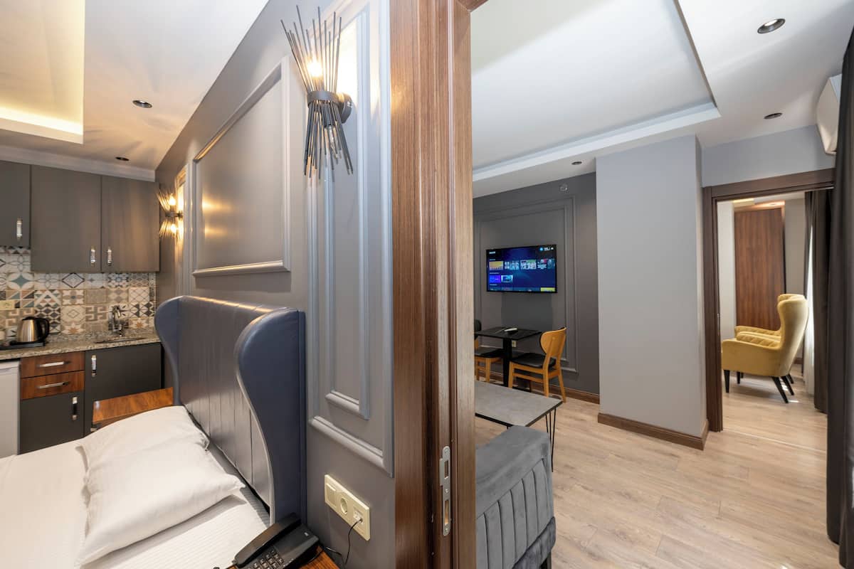 A modern hotel room with a bed, a TV, a dining area, and a kitchen.