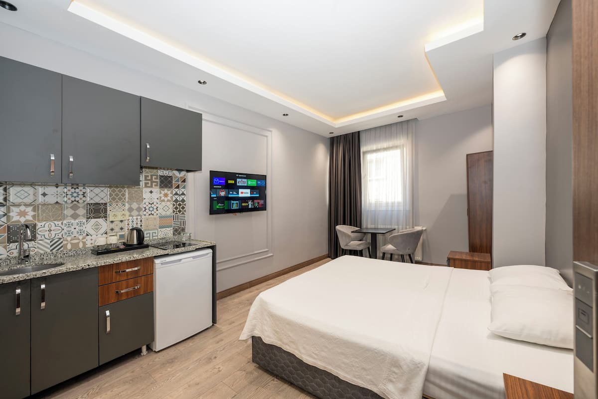 A modern hotel room with a kitchen area, a bed, a TV, and a small table with chairs.