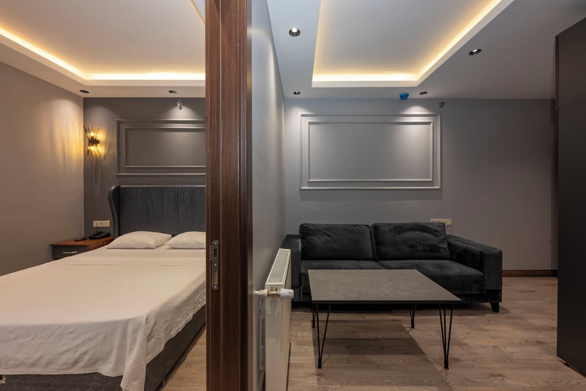 A modern hotel room with a bed, a sofa, a small table, and a wall-mounted TV.