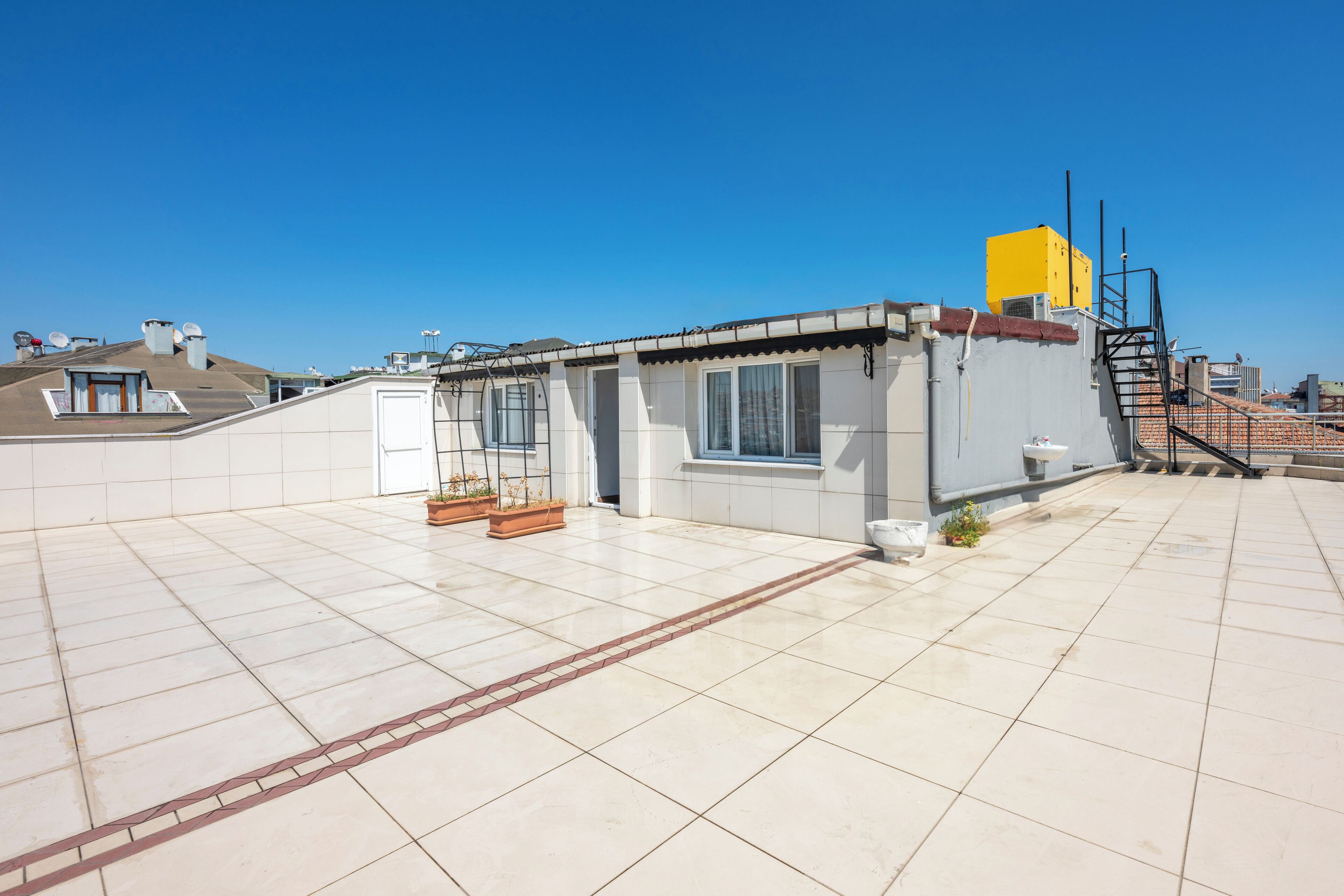 A rooftop terrace with a small building, a yellow air conditioning unit, and a staircase.