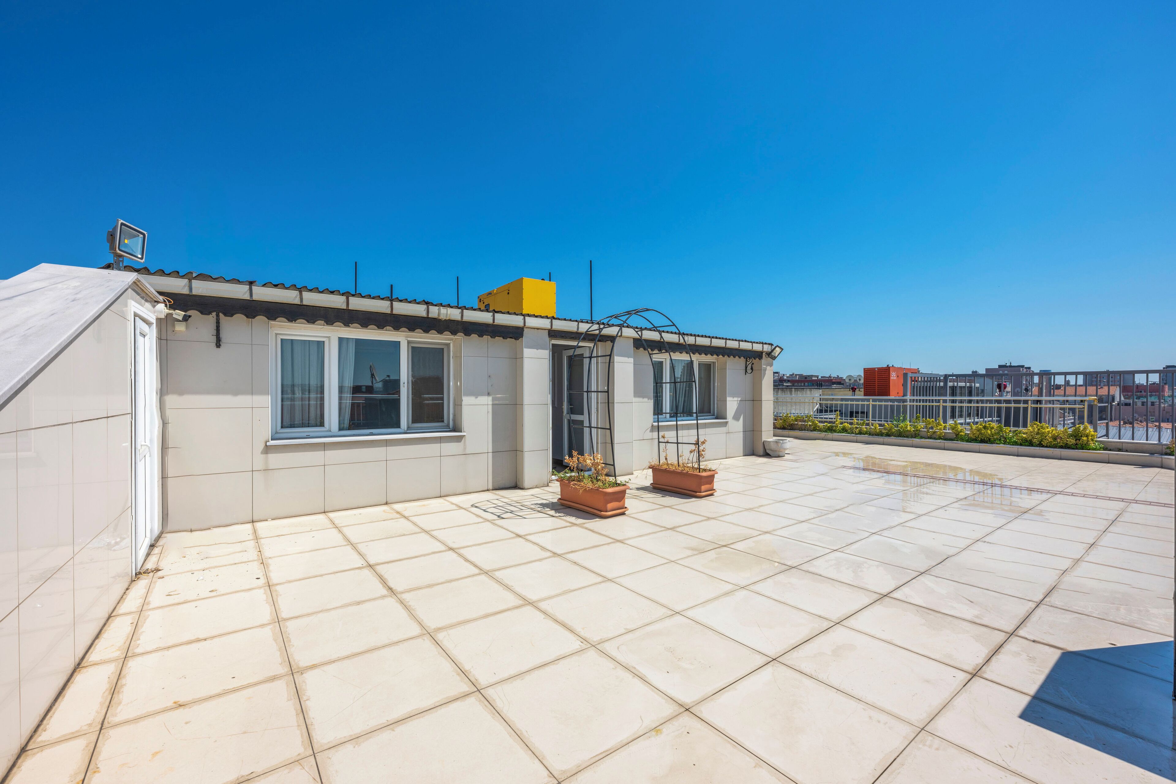 A rooftop terrace with tiled flooring, potted plants, and a clear view of the city skyline.