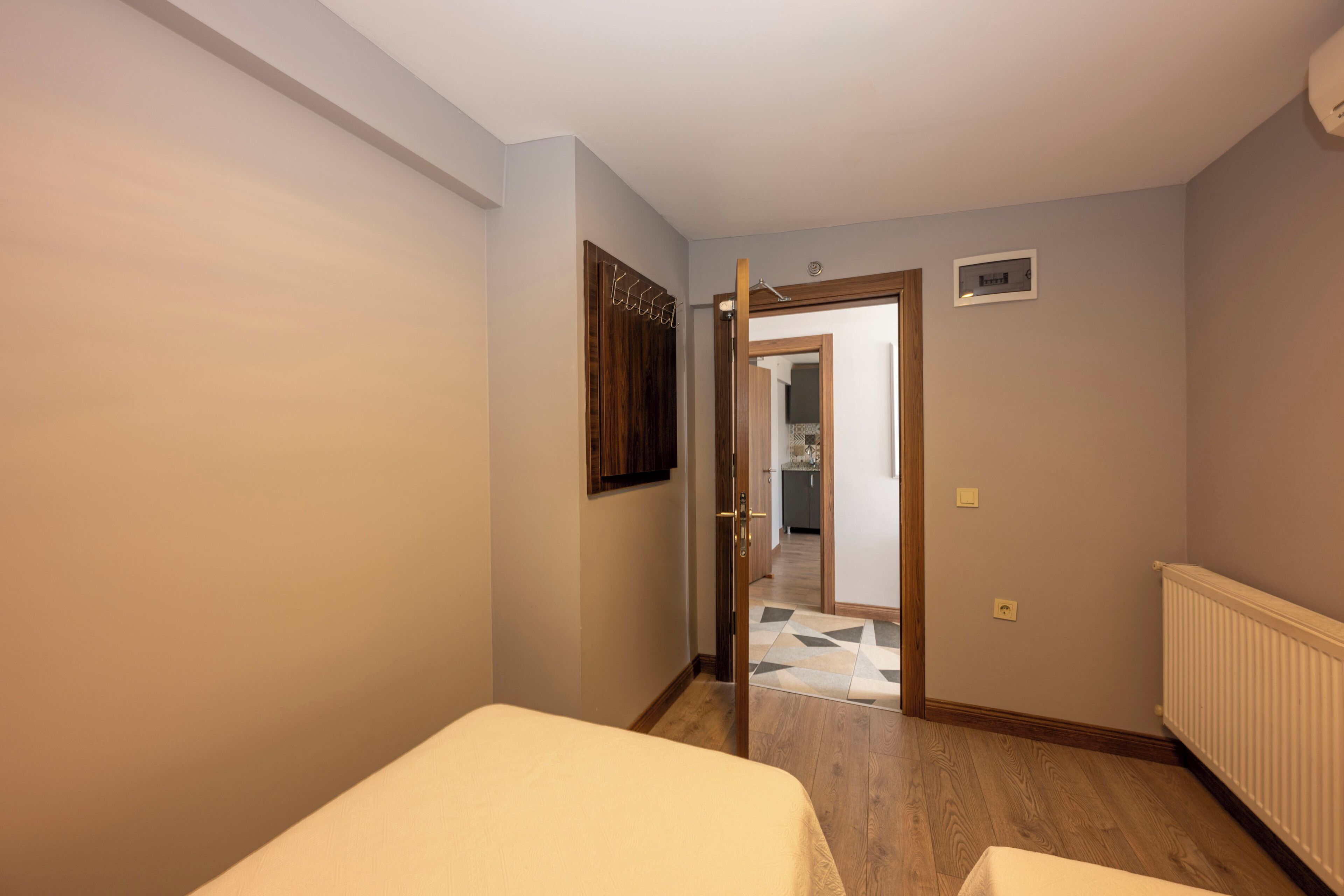 A bedroom with a bed, a wooden door, and a hallway leading to a kitchen.