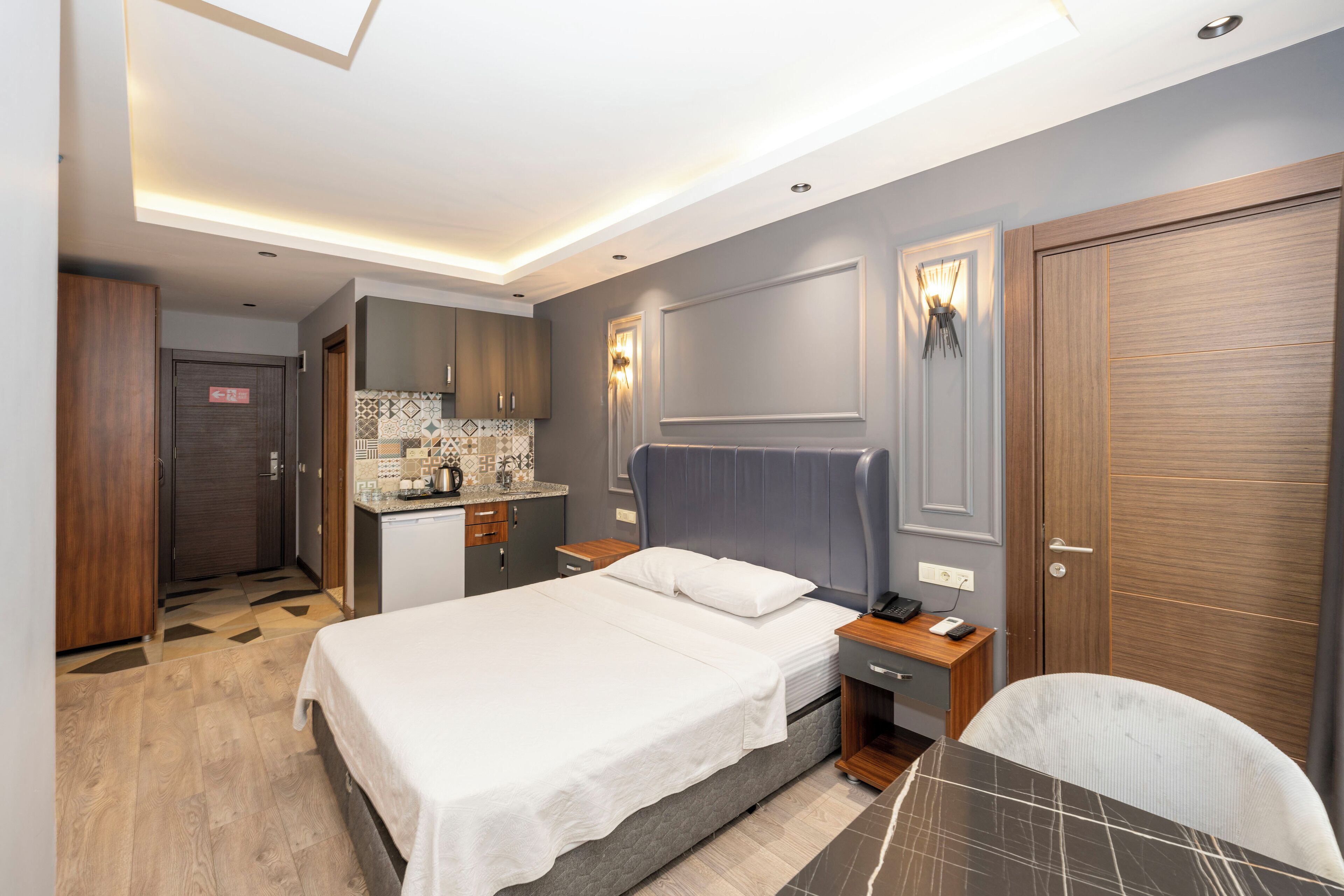 Quarto de hotel moderno com cama, mesa de cabeceira e pequena área de trabalho.