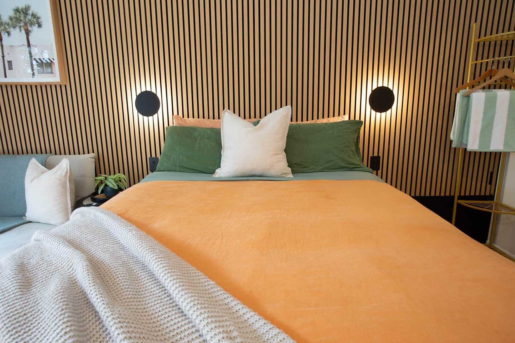 Een moderne slaapkamer met een lattenhouten hoofdbord, een bed met een oranje sprei en twee kussens.