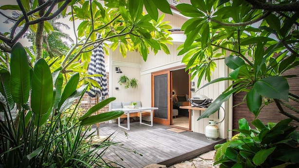 A patio with a table and chairs, surrounded by lush greenery and a wooden deck. - Alcorn Garden-Dog friendly 2 mins walk to beach (Suffolk Park)