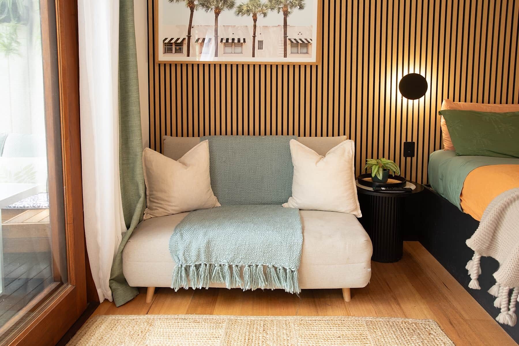 Ein gemütliches Schlafzimmer mit Bett, Sofa, einem kleinen Tisch mit Pflanze und einem gerahmten Bild an der Wand.
