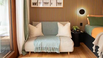 Ein gemütliches Schlafzimmer mit Bett, Sofa, einem kleinen Tisch mit Pflanze und einem gerahmten Bild an der Wand.