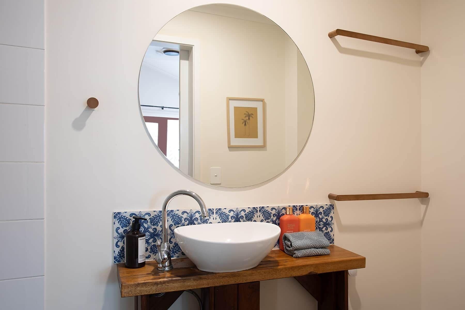 Un baño con espejo redondo, lavabo blanco y tocador de madera.