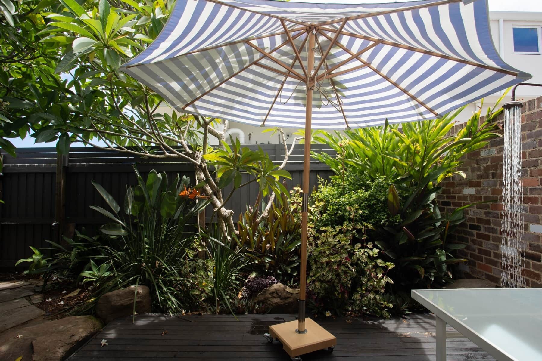 A patio area with a striped umbrella, a table, and various plants.