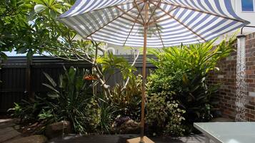 A patio area with a striped umbrella, a table, and various plants.