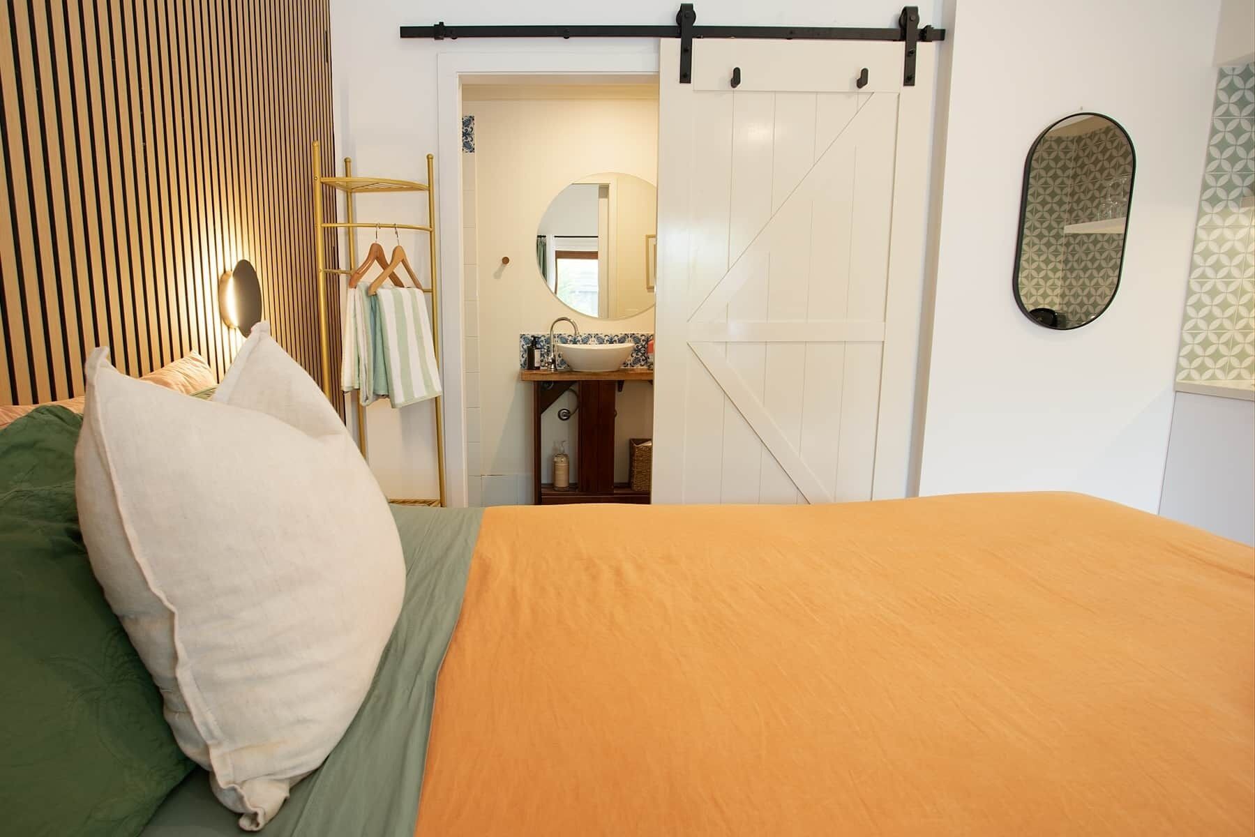 Un dormitorio con cama, armario, espejo y baño visible a través de una puerta abierta.