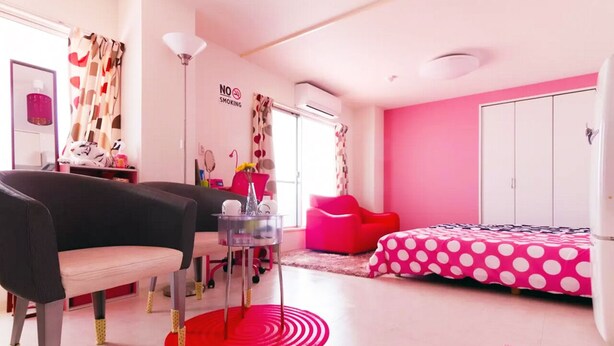 Una stanza a tema rosa e bianco con un letto, una sedia, un tavolino e un armadio.