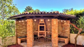 Patio esterno in mattoni con tetto in tegole, sedute in pietra e barbecue integrato.
