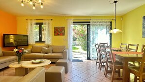 Un soggiorno con divano, poggiapiedi e televisore. C'è anche un'area pranzo con tavolo e sedie.