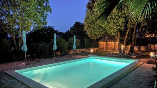 Una piscina rettangolare con bordi in pietra, circondata da alberi e mobili da esterno.