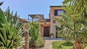 Una villa con un vialetto in pietra che conduce all'ingresso, circondata da piante tropicali e un cielo azzurro intenso.