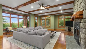 Ein geräumiges Wohnzimmer mit einem großen, grauen Ecksofa, einem Kamin aus Stein und einem Deckenventilator.