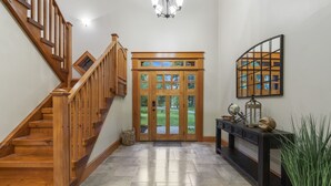 Eine Holztreppe führt zu einer Tür mit bleiverglasten Fenstern, ein Konsolentisch mit Dekorationsobjekten und ein großer Blumentopf.