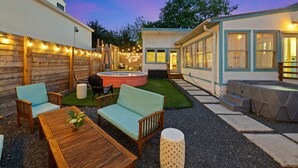 A patio area with outdoor furniture, a hot tub, and a building with large windows. - Boho-Ranch Retreat in Hip East Austin w Hot Tub and Cowgirl pool. (Austin)