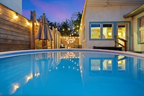 Una piscina con luces de cuerda, terraza de madera y un edificio con un letrero de neón.