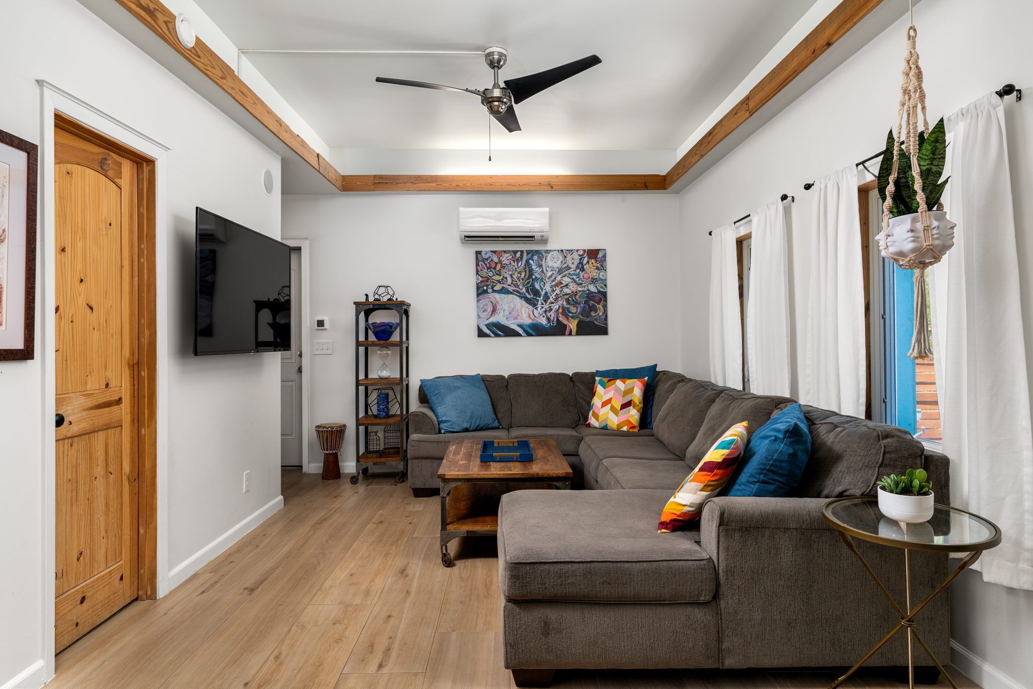 Un salon moderne avec un canapé d’angle, une table basse, un téléviseur et un ventilateur de plafond.