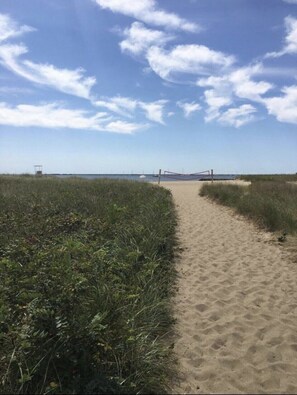 A sandy path leading to a beach with a lifeguard tower in the distance.