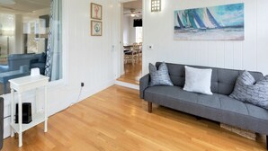 Ein Wohnzimmer mit grauem Sofa, Holzboden, einem weißen Tisch und einem Gemälde mit Segelbooten.