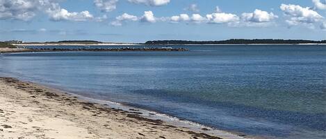 Une plage à l’eau claire, avec un rivage sablonneux et un promontoire rocheux visible au loin.
