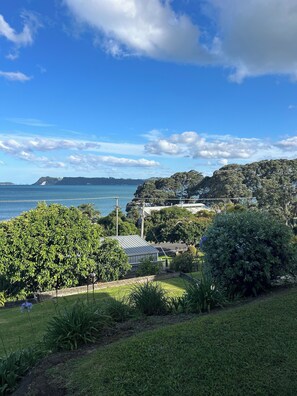 A coastal landscape with a view of the sea, greenery, and a building with a sloped roof. - Simpson's Beach - Fantastic View - Beach Home (Whitianga)
