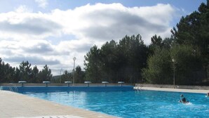 En swimmingpool med kristallklart blått vatten, omgiven av träd och en molnig himmel.