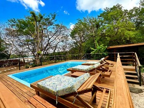 A wooden deck with a swimming pool, lounge chairs, and a wooden pergola.