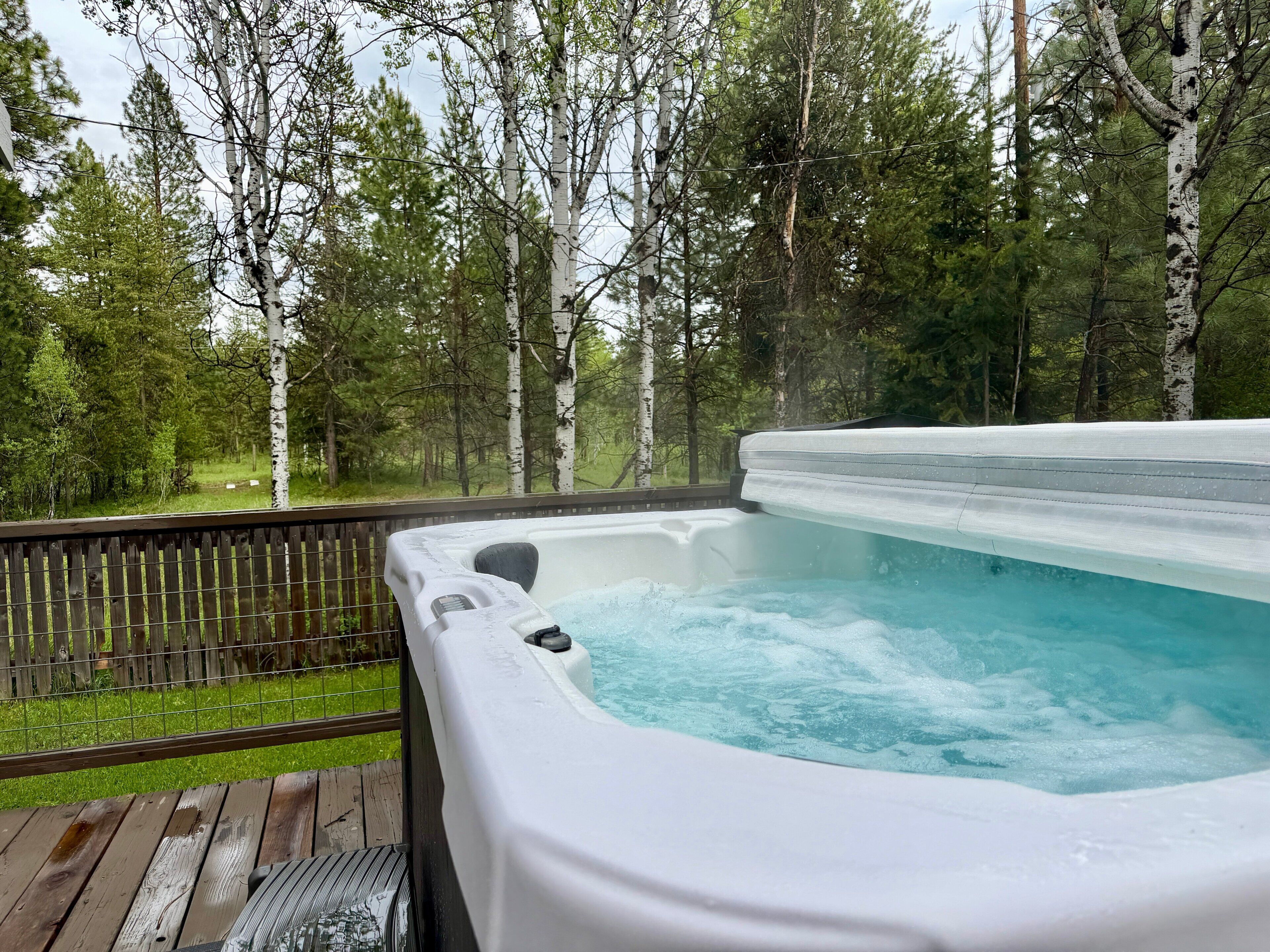 Ett bubbelbad på ett trädäck med en skog i bakgrunden.
