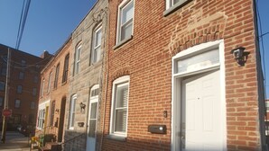 Une rangée de maisons de ville en briques, avec des portes et des fenêtres blanches, une boîte aux lettres bien visible et un panneau de signalisation sur le trottoir.