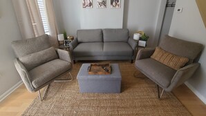 Un salon avec un canapé gris, deux fauteuils, une table basse et trois tableaux accrochés au mur.