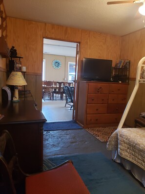 A room with a wooden floor, a television on a dresser, a clock on the wall, and a door leading to another room.