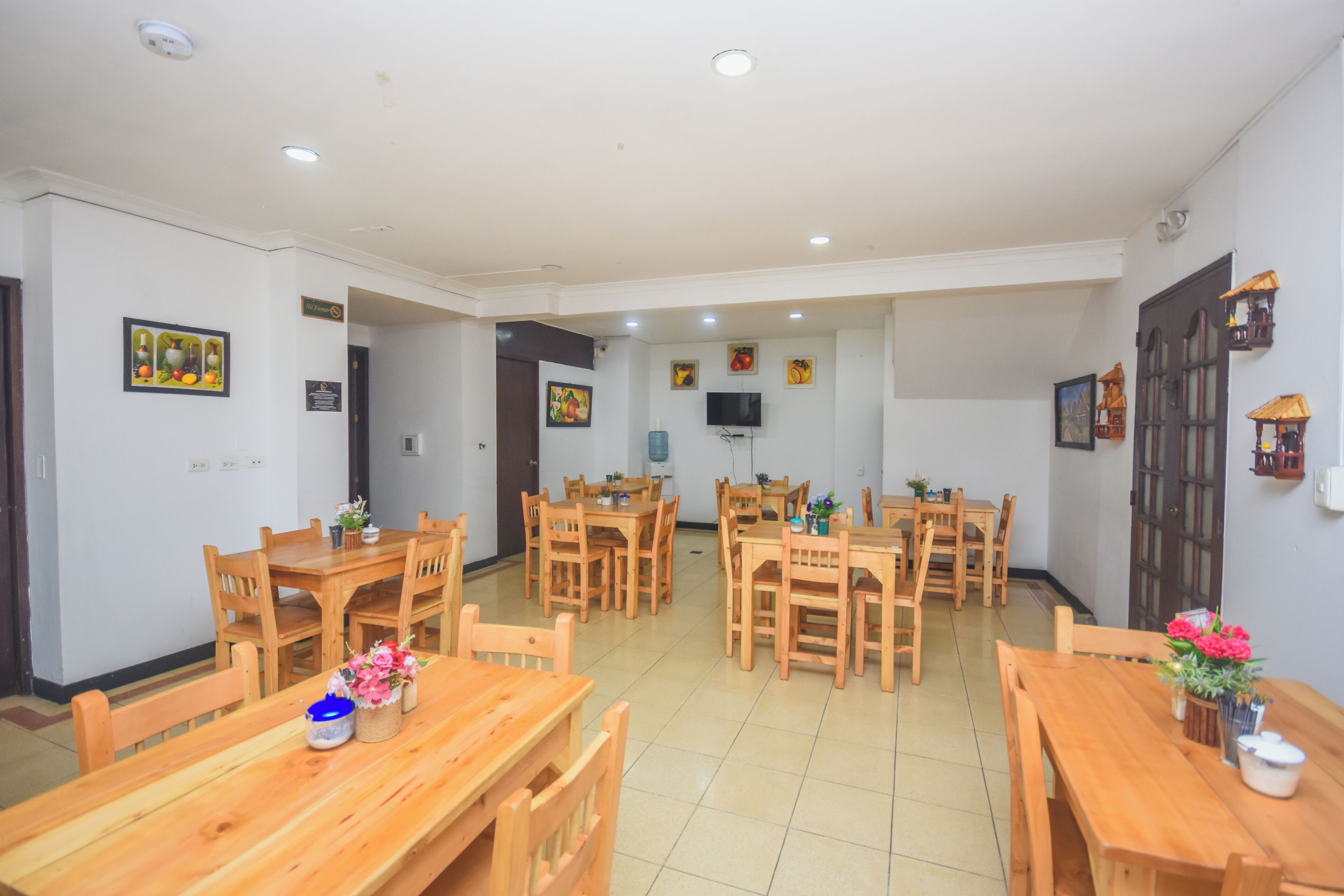 Un grand espace dédié à la salle à manger, avec de nombreuses tables et chaises en bois, un téléviseur fixé au mur et divers éléments de décoration murale.