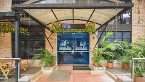 L’entrée d’un hôtel, avec un patio couvert, des plantes en pot et un panneau numérique affichant le nom « ERTO ».