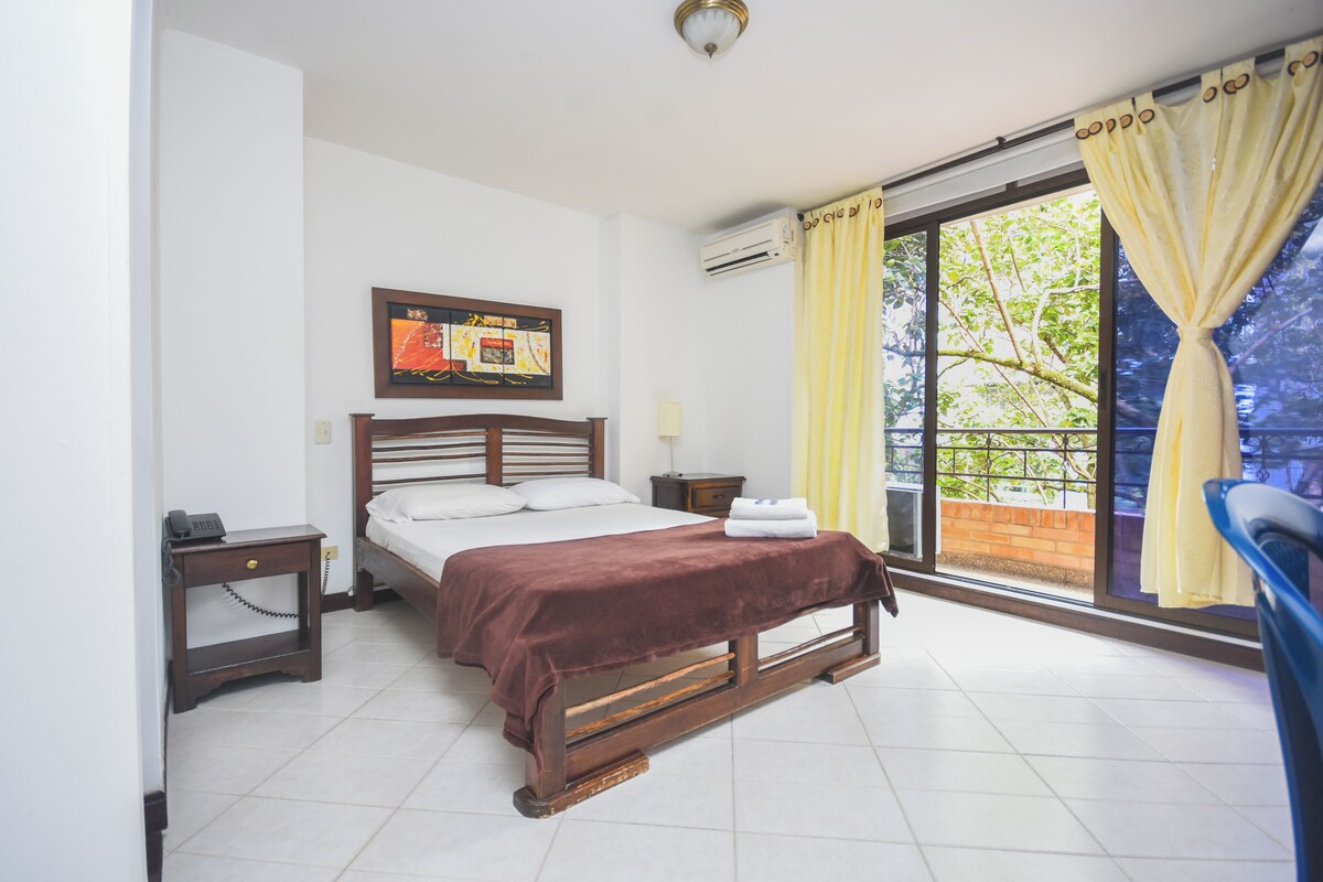Un dormitorio con cama, mesitas de noche, aire acondicionado en la pared y una ventana con cortinas.