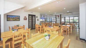 Un vaste espace dédié à la salle à manger, avec de nombreuses tables et chaises en bois, une grande peinture au mur et une vue par les fenêtres.