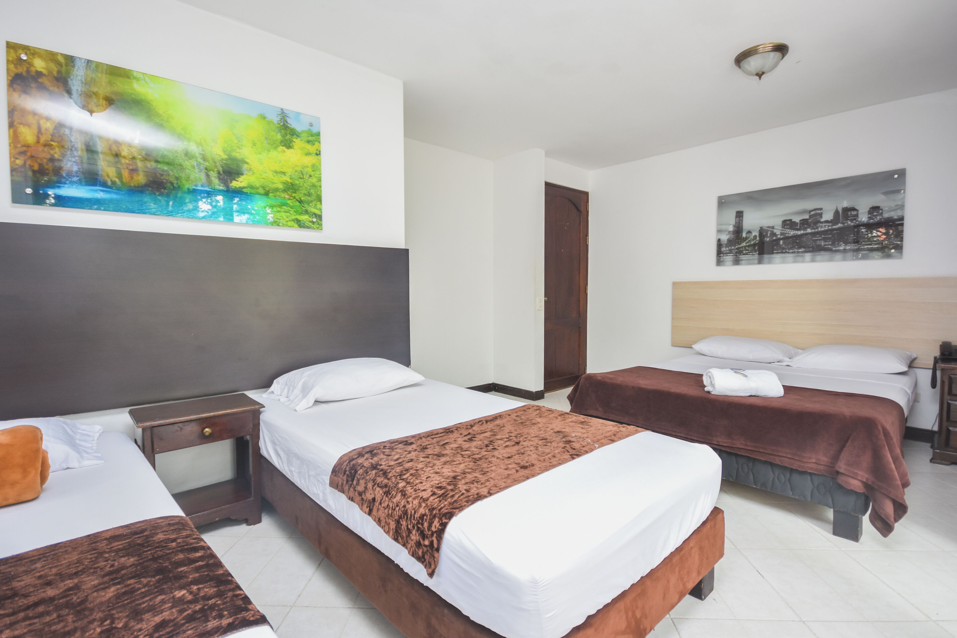 A hotel room with two beds, a large painting of a waterfall, a cityscape, and a wooden headboard.