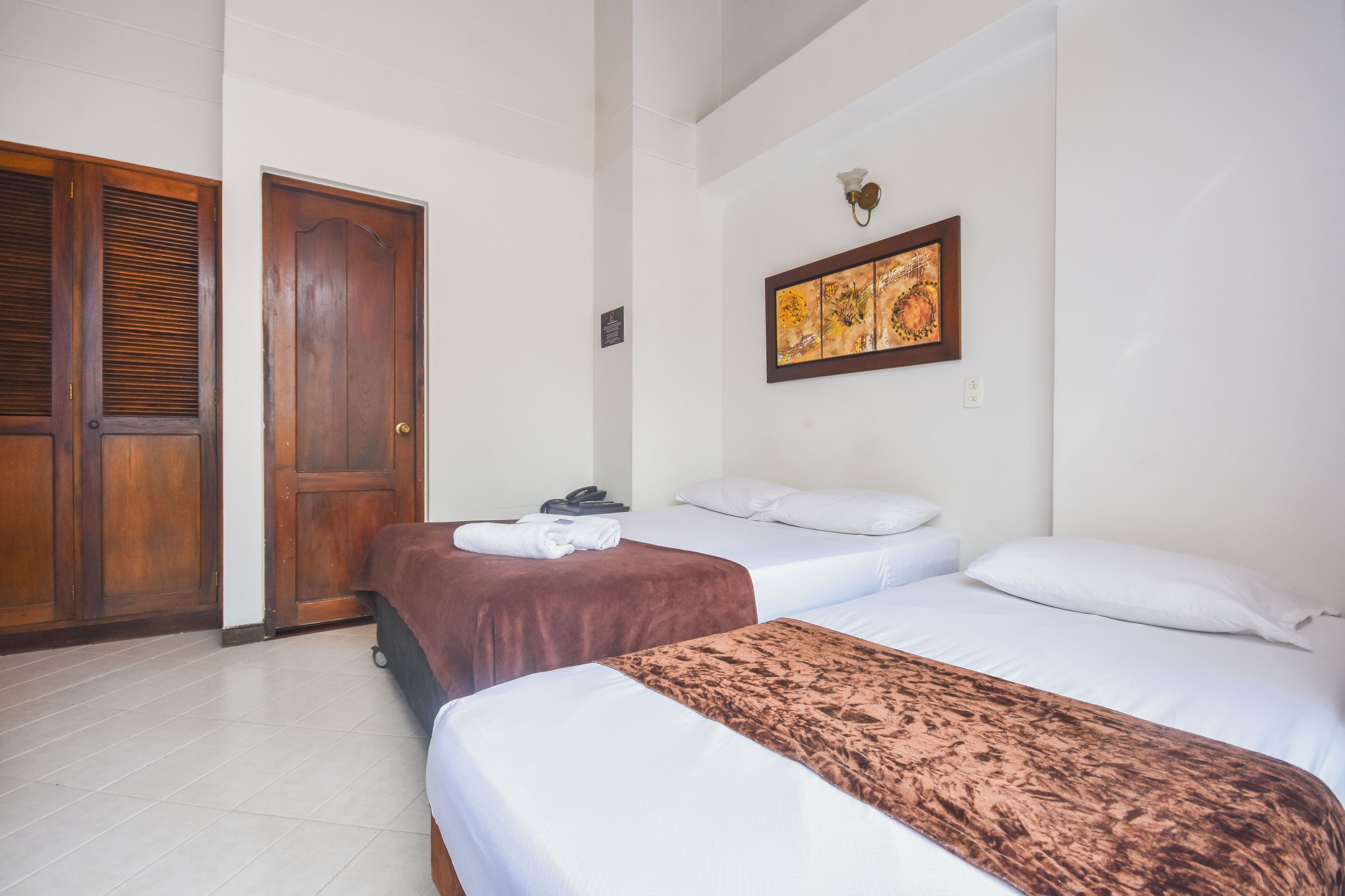 Una habitación de hotel con dos camas, una puerta de madera y una obra de arte enmarcada en la pared.