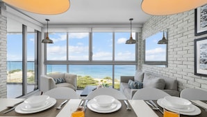 Een eetruimte met een tafel gedekt voor twee personen, grote ramen met uitzicht op zee, en een bakstenen muur.