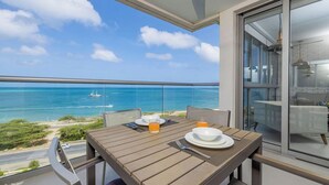 Een balkon met een tafel voor twee, met uitzicht op een strand en een heldere blauwe lucht en zee.
