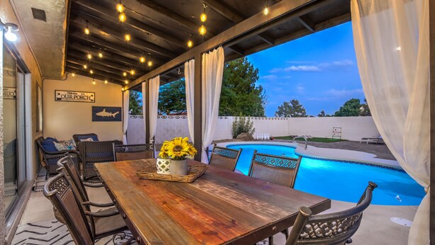 Eine Terrasse im Freien mit einem Holztisch, Stühlen, einem Pool und einem Schild mit der Aufschrift 'Welcome to Our Porch'.