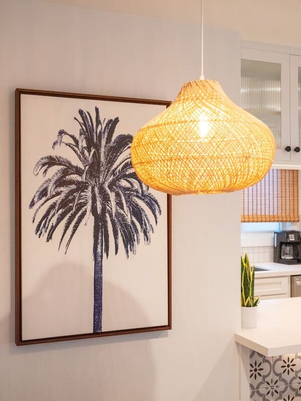 Una obra de arte en blanco y negro con una palmera en un marco, una lámpara colgante de mimbre y una cocina con cafetera.