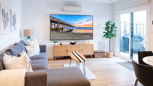 Un soggiorno moderno con una TV a schermo piatto, un divano grigio, un mobiletto in legno e un'area pranzo con tavolo e sedie.