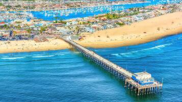 A pier extending into the sea with a boat docked at the end, surrounded by a beach and a coastal town.
